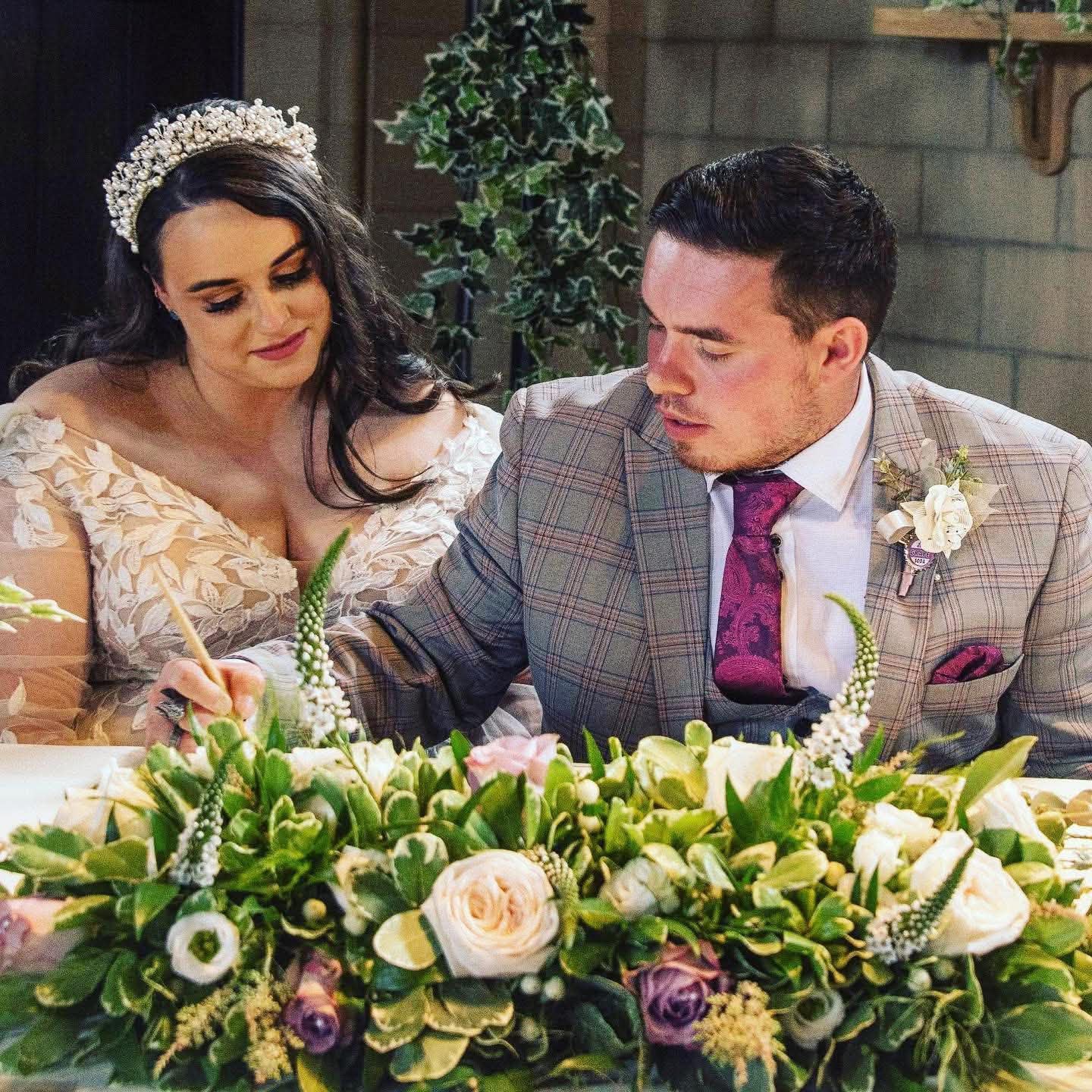 Newlyweds seated behind a floral top-table arrangement